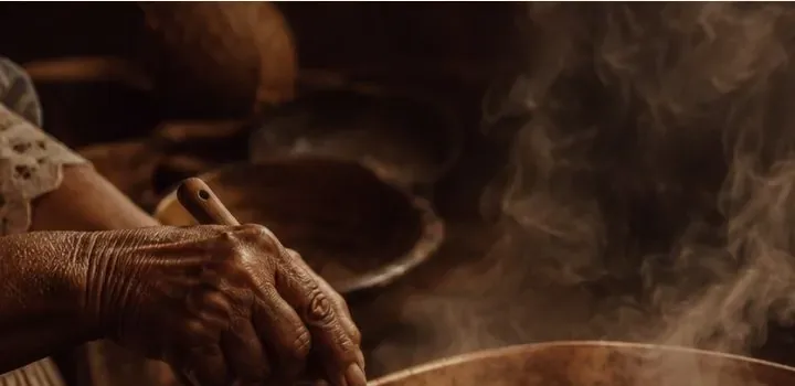 Mãos mexendo a cocada no tacho de cobre, com vapor subindo